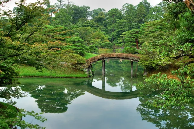 Pont en pierre arqué enjambant un étang calme entouré de végétation luxuriante à Kyoto