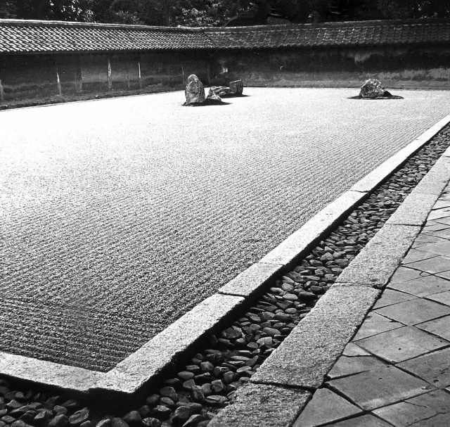 Jardin zen japonais avec pierres disposées sur gravier ratissé et murs en pierre