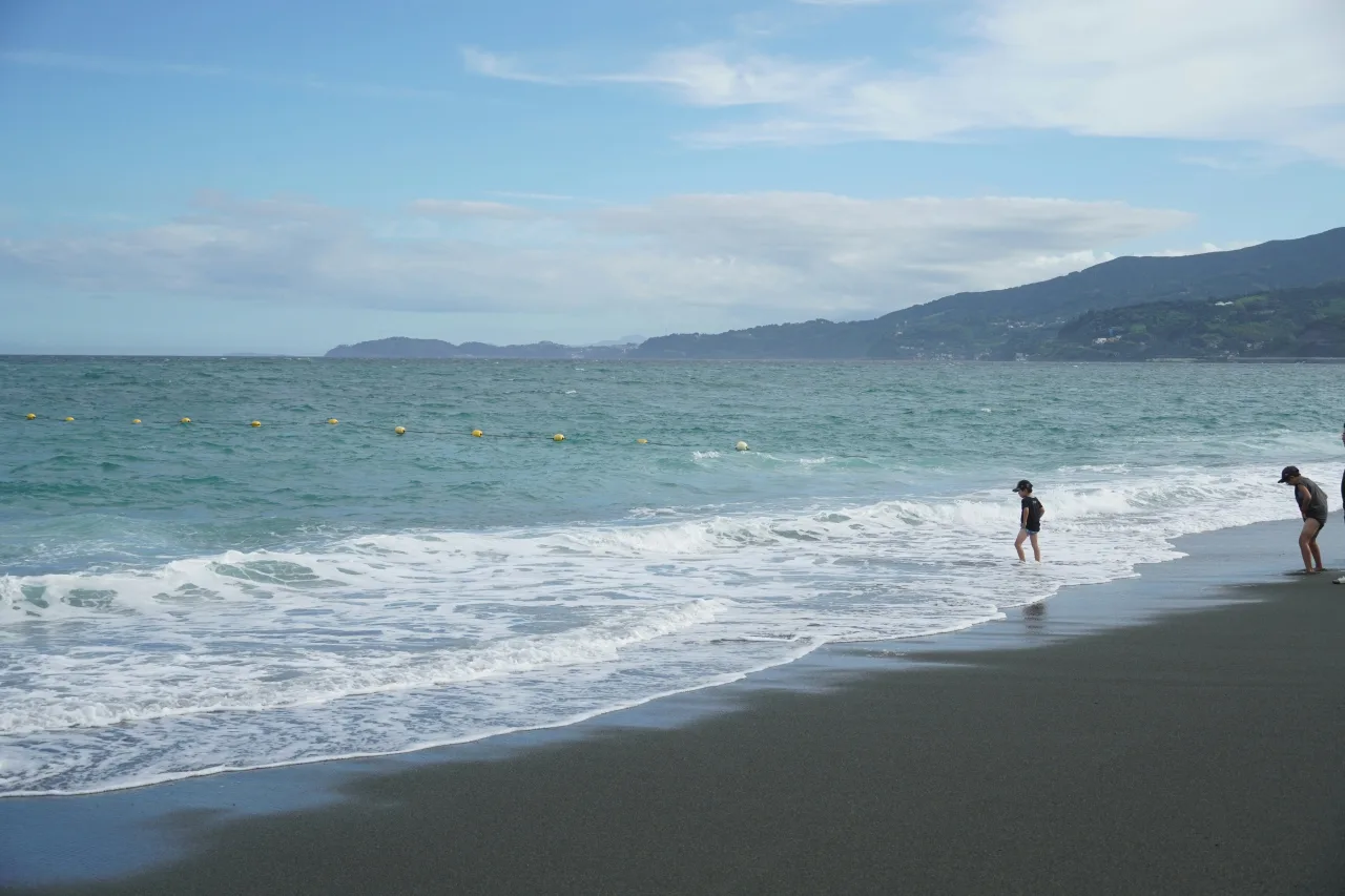 Plage japonaise avec baigneurs, vagues turquoise et montagnes boisées en arrière-plan