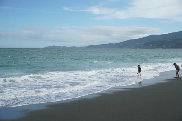 Plage japonaise avec baigneurs, vagues turquoise et montagnes boisées en arrière-plan