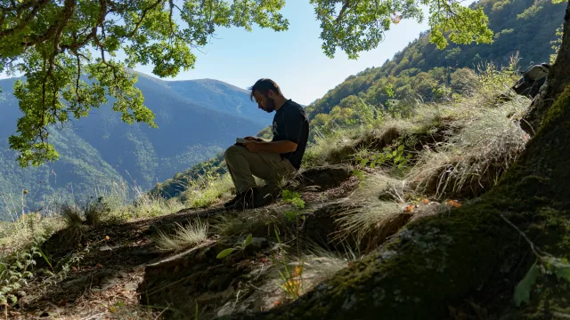 Randonneur assis sur un sentier de montagne forestier avec vue sur une vallée boisée