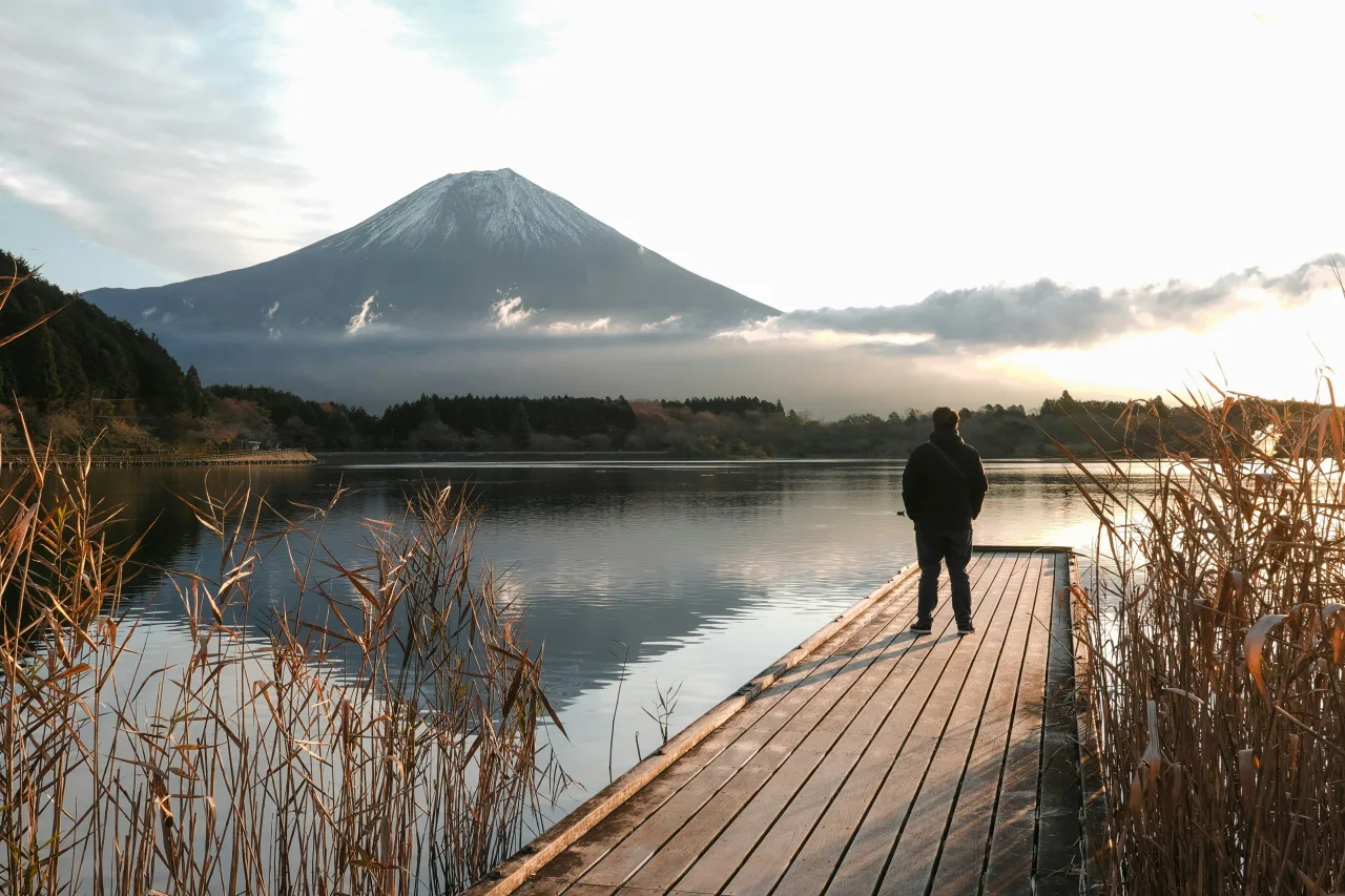 Homme sur une jetée face au Mont Fuji enneigé se reflétant dans le lac au Japon