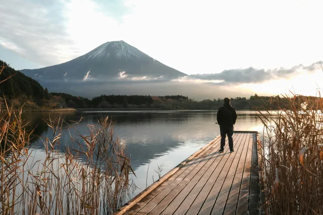 Homme sur une jetée face au Mont Fuji enneigé se reflétant dans le lac au Japon
